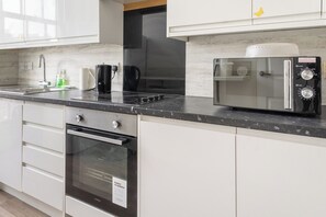 A modern kitchen with white cabinetry, a built-in oven, a microwave, and a coffee maker. - Stylish 2-Bed Flat in Edinburgh with Great Views (Edinburgh)