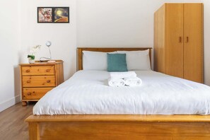 Una cama bien hecha con sábanas blancas, una almohada color turquesa y toallas dobladas sobre un cabecero de madera.