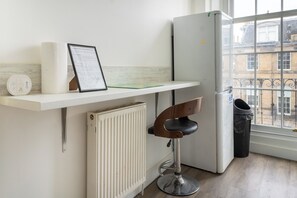 A kitchen with a white countertop, a white radiator, a black trash bin, and a window with a view of buildings. - Stylish 2-Bed Flat in Edinburgh with Great Views (Edinburgh)