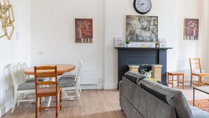 A living room with a round wooden table, white chairs, a grey sofa, and a fireplace. - Stylish 2-Bed Flat in Edinburgh with Great Views (Edinburgh)
