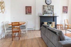 A living room with a round wooden table, white chairs, a grey sofa, and a fireplace. - Stylish 2-Bed Flat in Edinburgh with Great Views (Edinburgh)