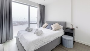 Camera d'albergo moderna con un letto grande, un comodino e vista sulla città attraverso ampie finestre.