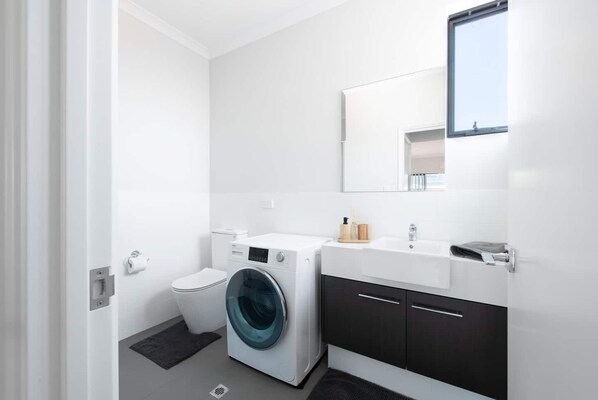 A modern bathroom with a washing machine, toilet, and a sink with a mirror above it.