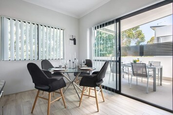 Elegant dining space with a glass-top table, stylish chairs, and access to a sunny balcony.