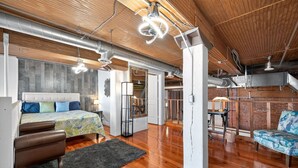 A spacious loft with exposed ductwork, a large bed, a sofa, and a staircase leading to an upper level. - Stylish Loft with Modern Amenities in Detroit (Detroit)