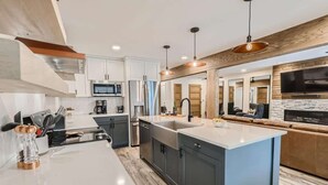 A modern kitchen with a central island, built-in appliances, and a large TV mounted on the wall.