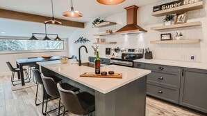 A modern kitchen with a central island, pendant lighting, and built-in shelving.