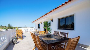 A terrace with a wooden table and chairs, a potted plant, and a view of the sea.