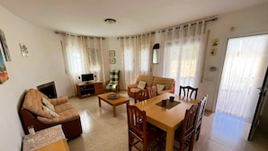 A living room with a sofa, a dining table with chairs, a TV stand, and a fireplace. - Villa Jane (Les Tres Cales)