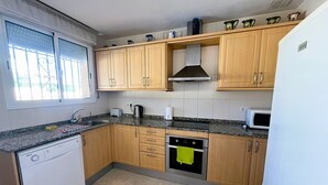 A kitchen with wooden cabinets, a built-in oven, a microwave, and a dishwasher. - Villa Jane (Les Tres Cales)