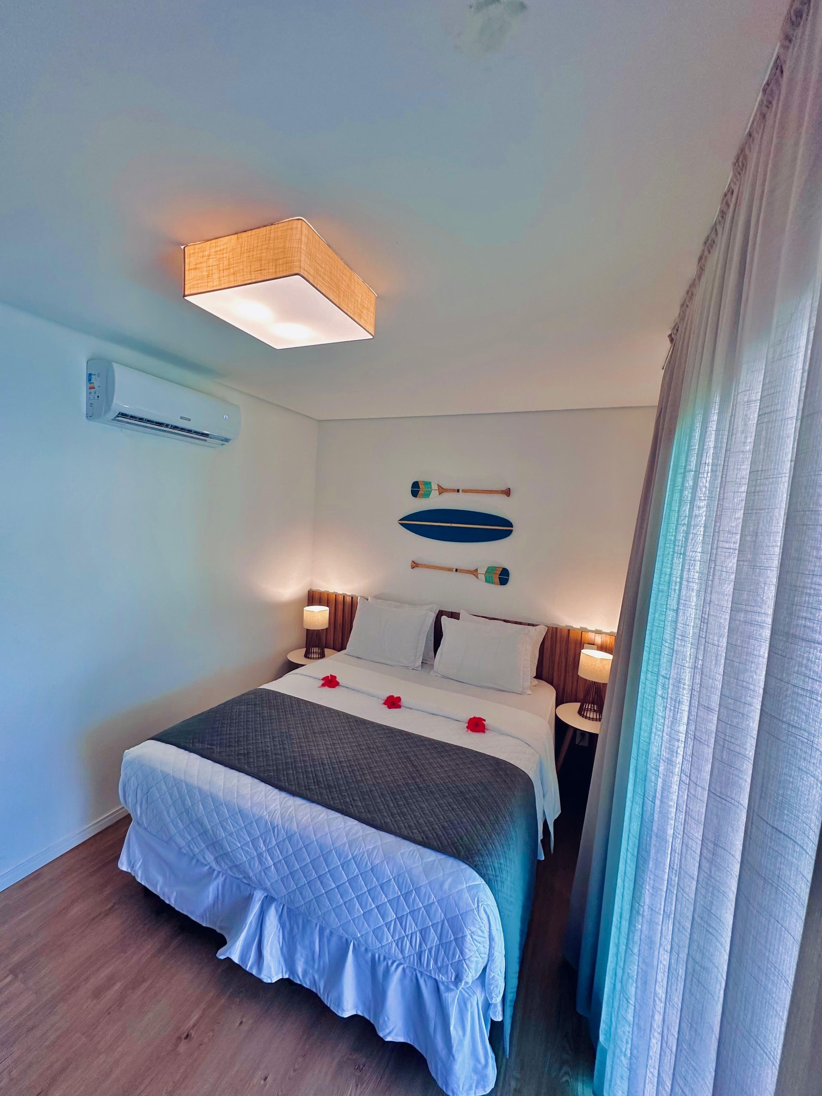 A neatly made double bed with a quilted cover, a wall-mounted air conditioner, and two wall-mounted lamps.