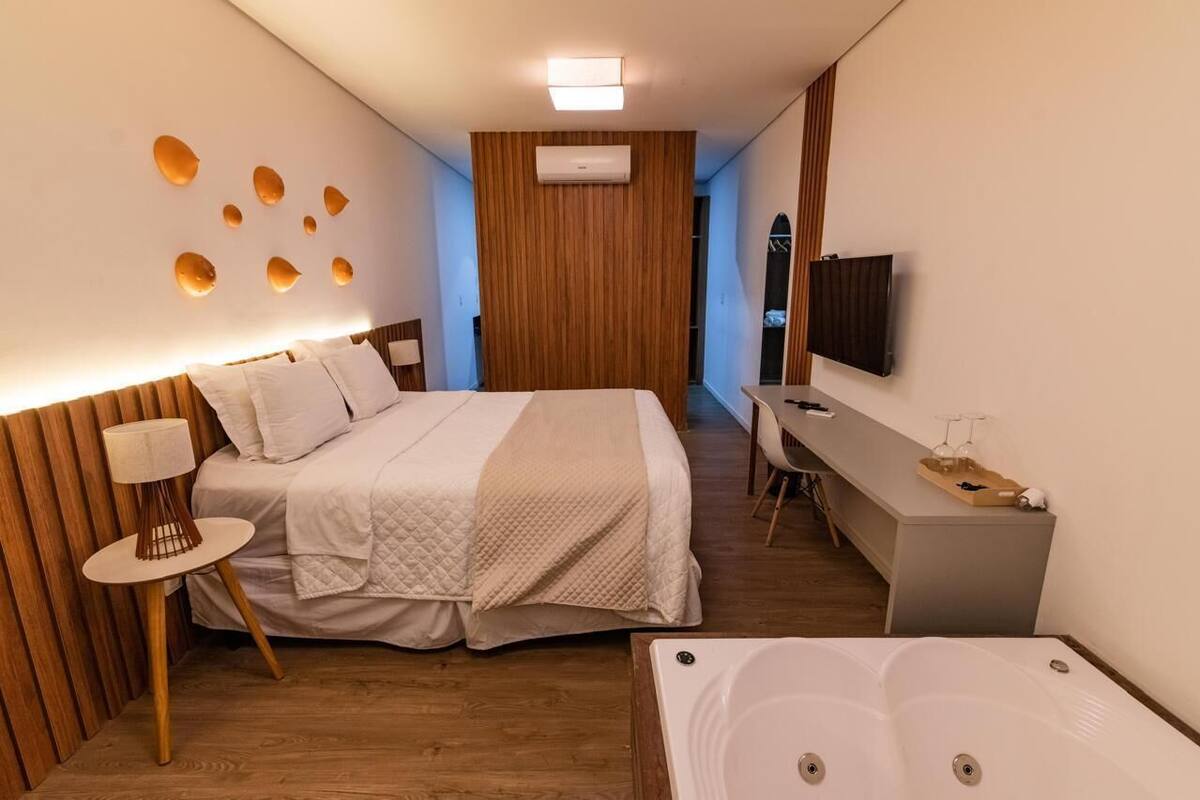 A modern hotel room with a large bed, a desk, a TV, and a bathtub.