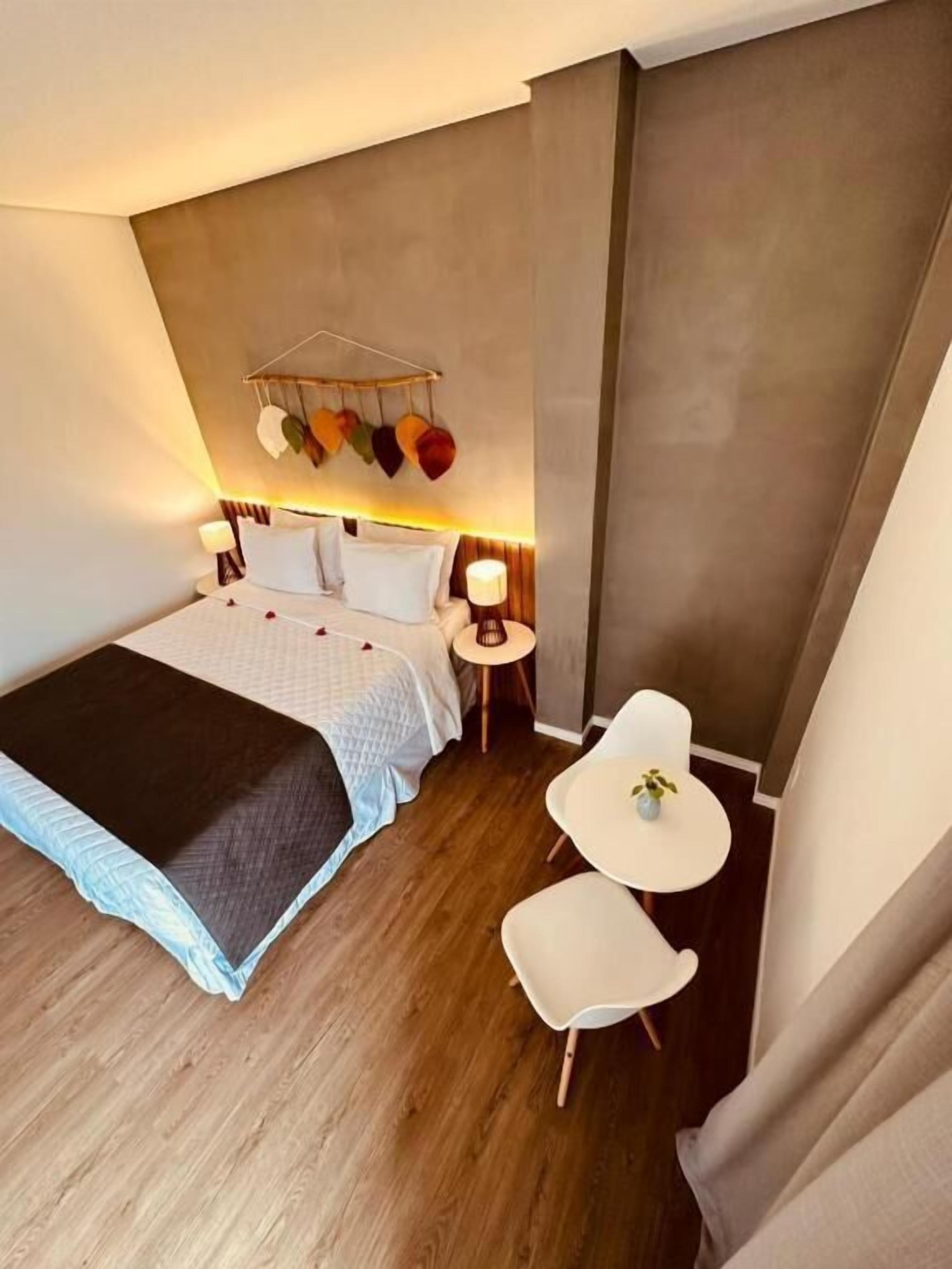 Una habitación de hotel moderna con una cama grande, mesitas de noche, una pequeña mesa redonda y una silla.