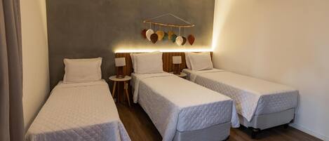 Une chambre d’hôtel avec trois lits simples, une table de chevet avec une lampe, un climatiseur fixé au mur et un objet décoratif suspendu.