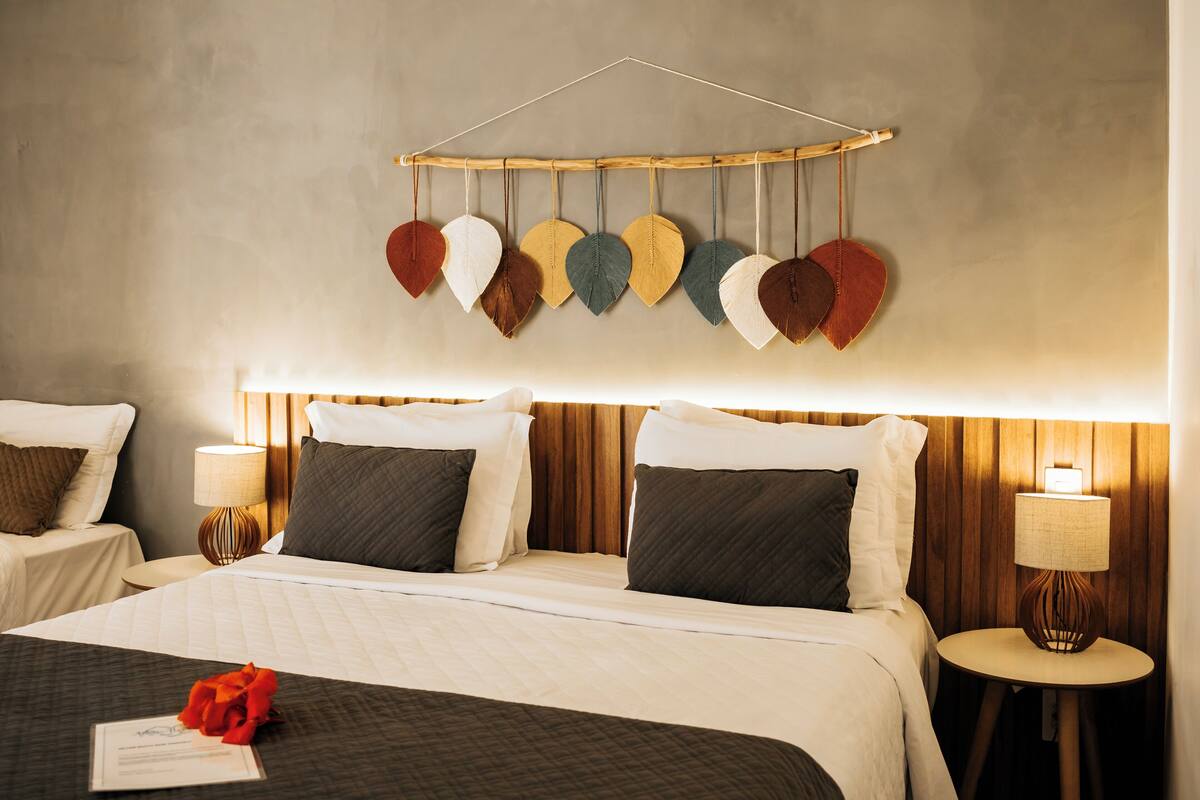 A hotel room with a bed, two bedside tables, a wall-mounted heart-shaped decoration, and a lamp.