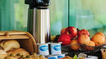 Un bufé de desayuno con diferentes alimentos, una cafetera y un bol de fruta.
