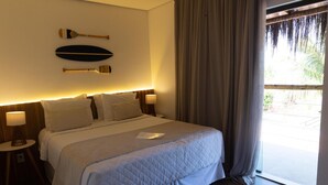 A hotel room with a large bed, two bedside tables, a wall-mounted paddleboard, and a view of the outdoors through a sliding door. - POUSADA AMAR NORONHA (Fernando de Noronha)