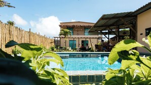 A pool area with a wooden fence, a building with a thatched roof, and a clear blue sky. - POUSADA AMAR NORONHA (Fernando de Noronha)