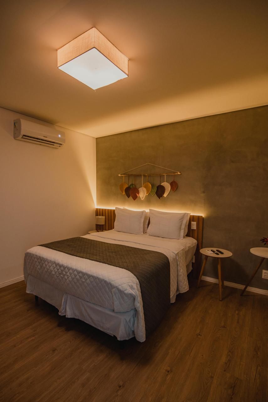 A hotel room with a bed, bedside tables, a wall-mounted air conditioner, and a ceiling light fixture.
