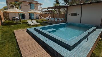 Piscina com deck de madeira, área de estar ao ar livre e guarda-sóis.