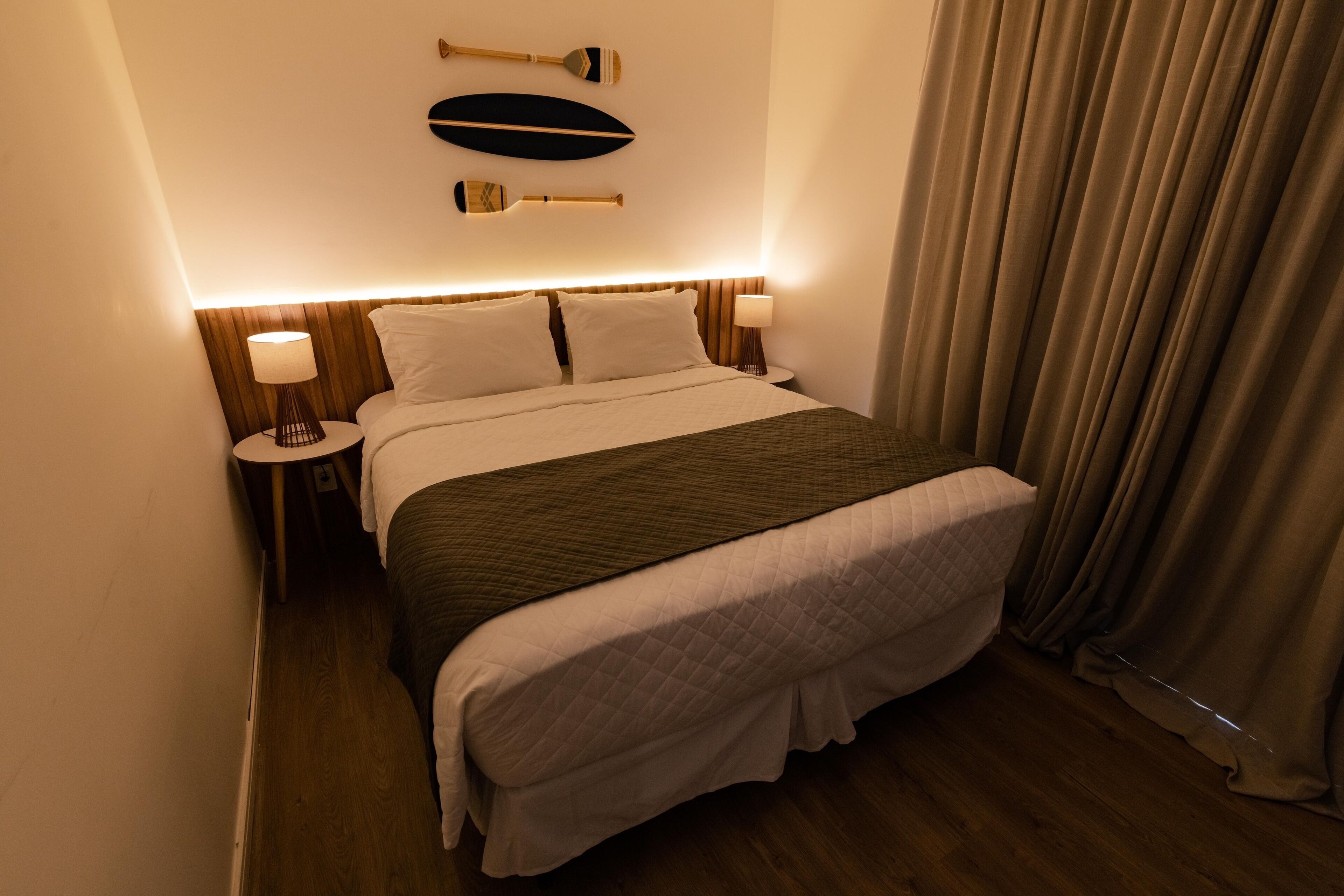 Una cama bien tendida con un cubrecolcha acolchado, dos lámparas de noche y un adorno en la pared.