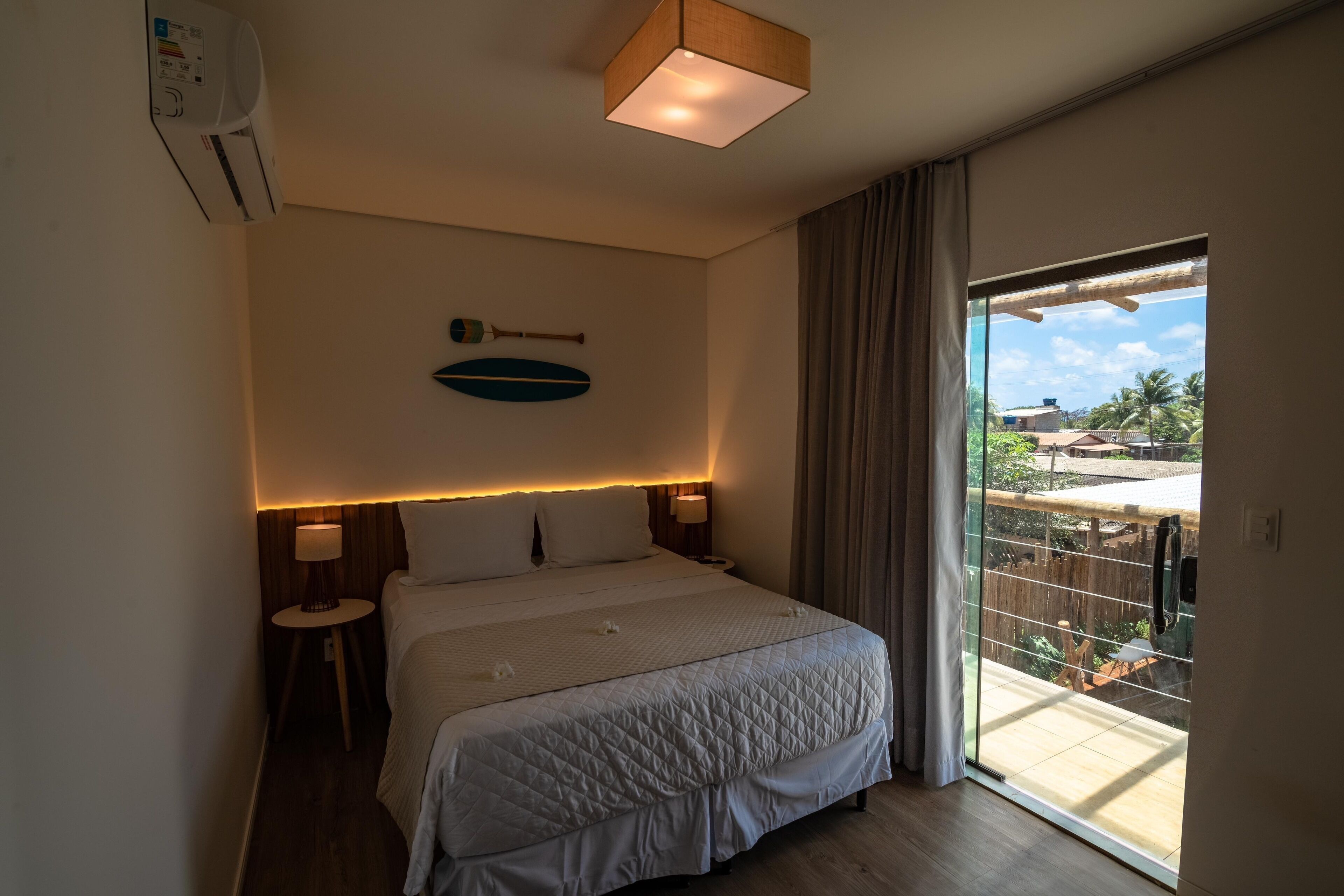 Habitación de hotel con una cama grande, una mesita de noche, un calefactor en la pared, una lámpara de techo y un balcón con vistas al exterior.
