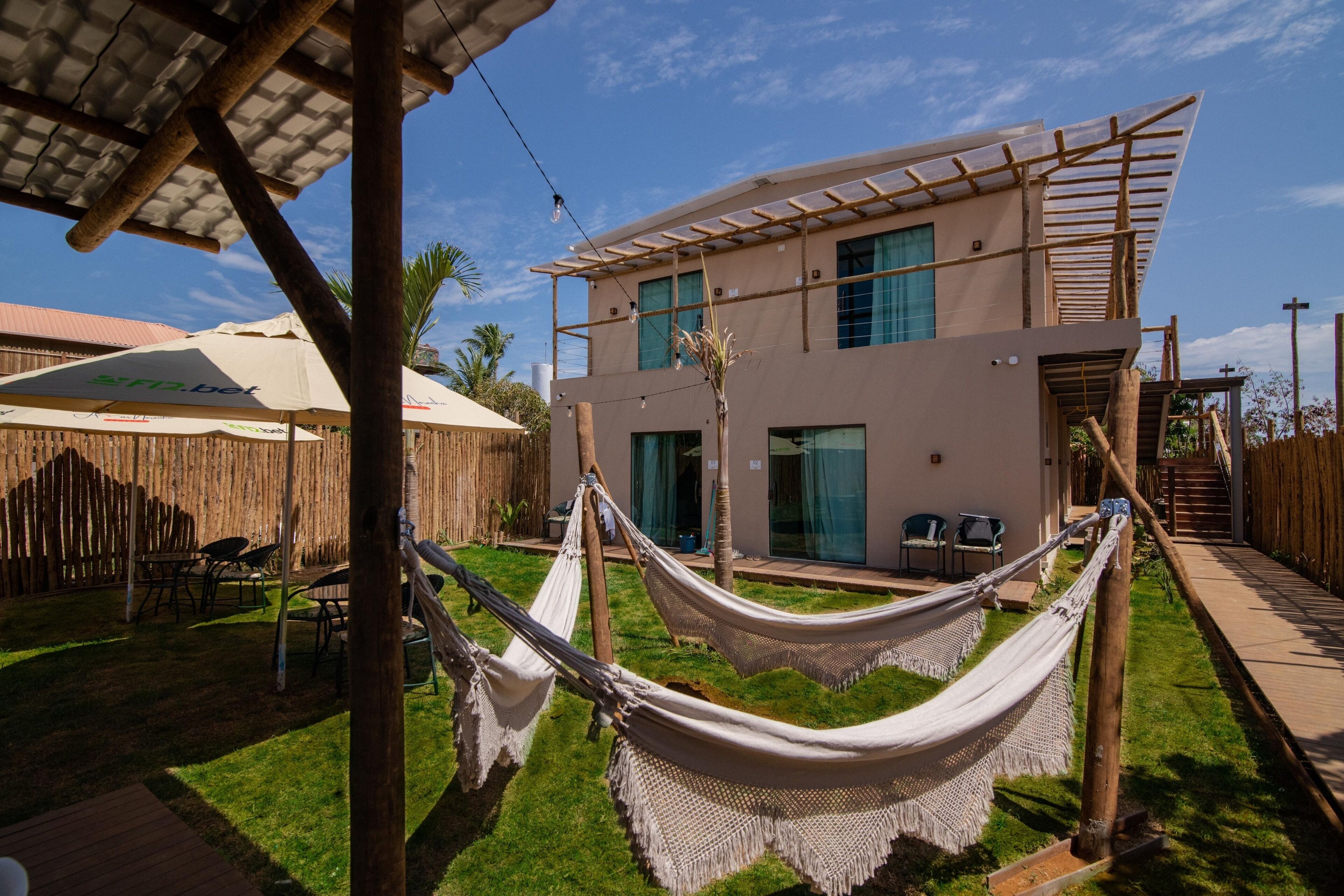A modern two-story house with a covered patio area, a hammock, and a wooden fence.