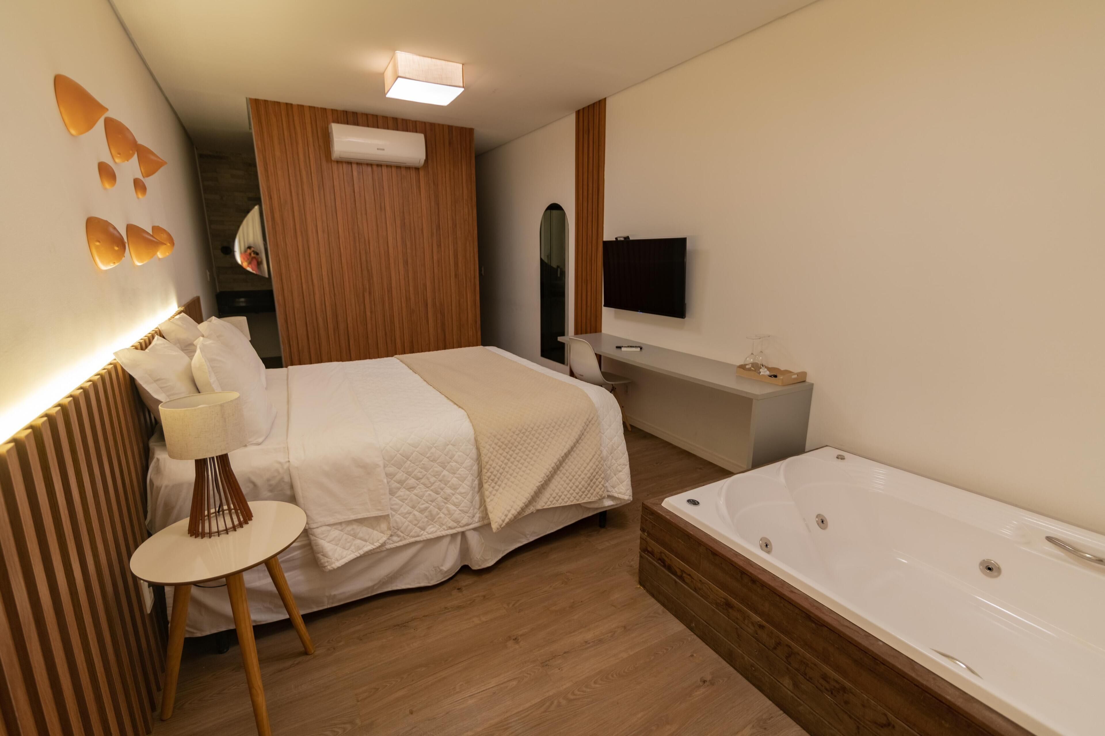 A modern hotel room with a large bed, a small round table, a bathtub, and a TV mounted on the wall.