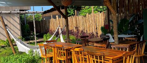 An outdoor wooden deck with tables and chairs, a hammock, and a bamboo fence.