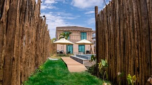 A pathway leading to a building with a modern design, a wooden fence on either side, and a clear blue sky. - POUSADA AMAR NORONHA (Fernando de Noronha)