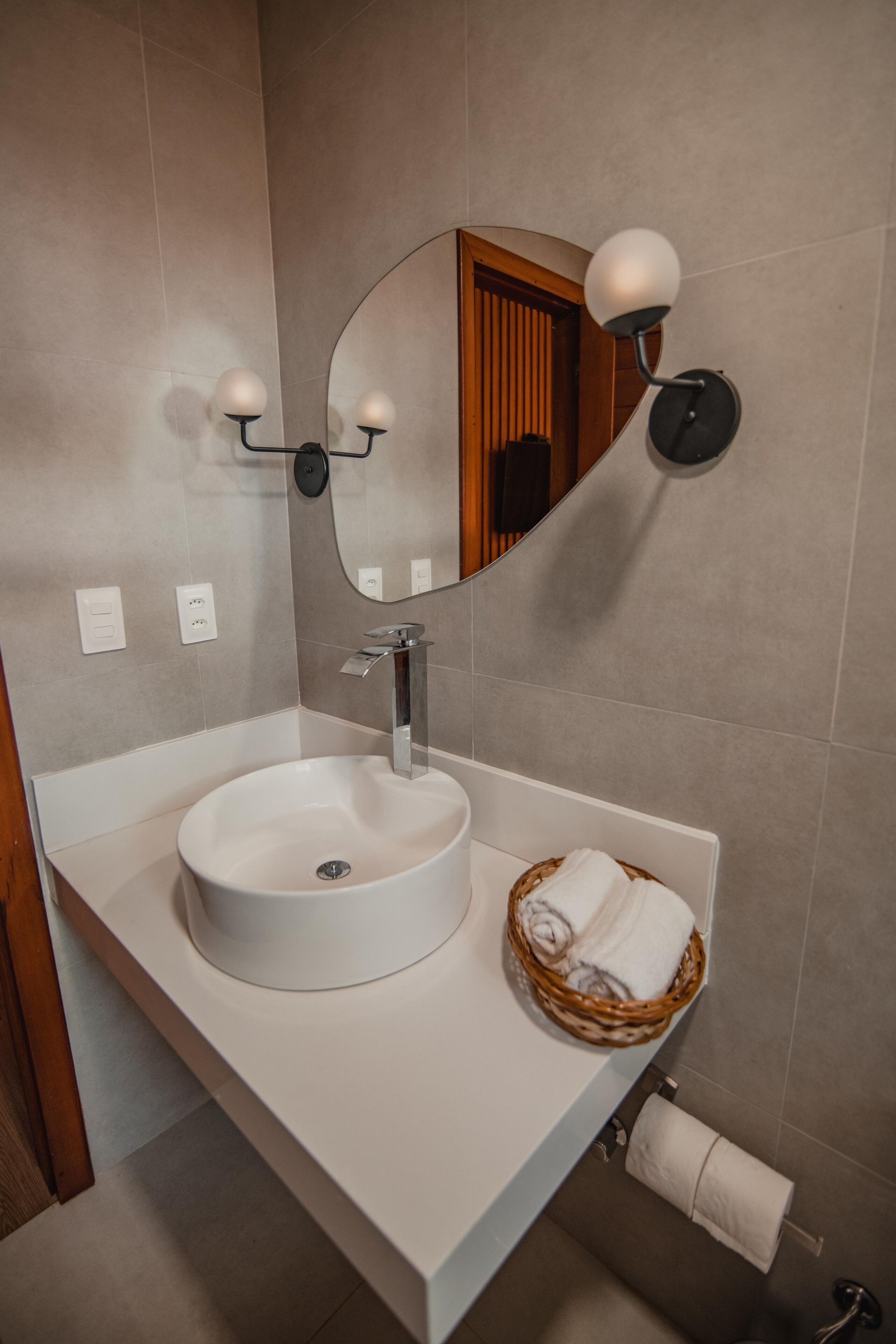 Een badkamer met een witte wasbak, een spiegel en een mand voor handdoeken.