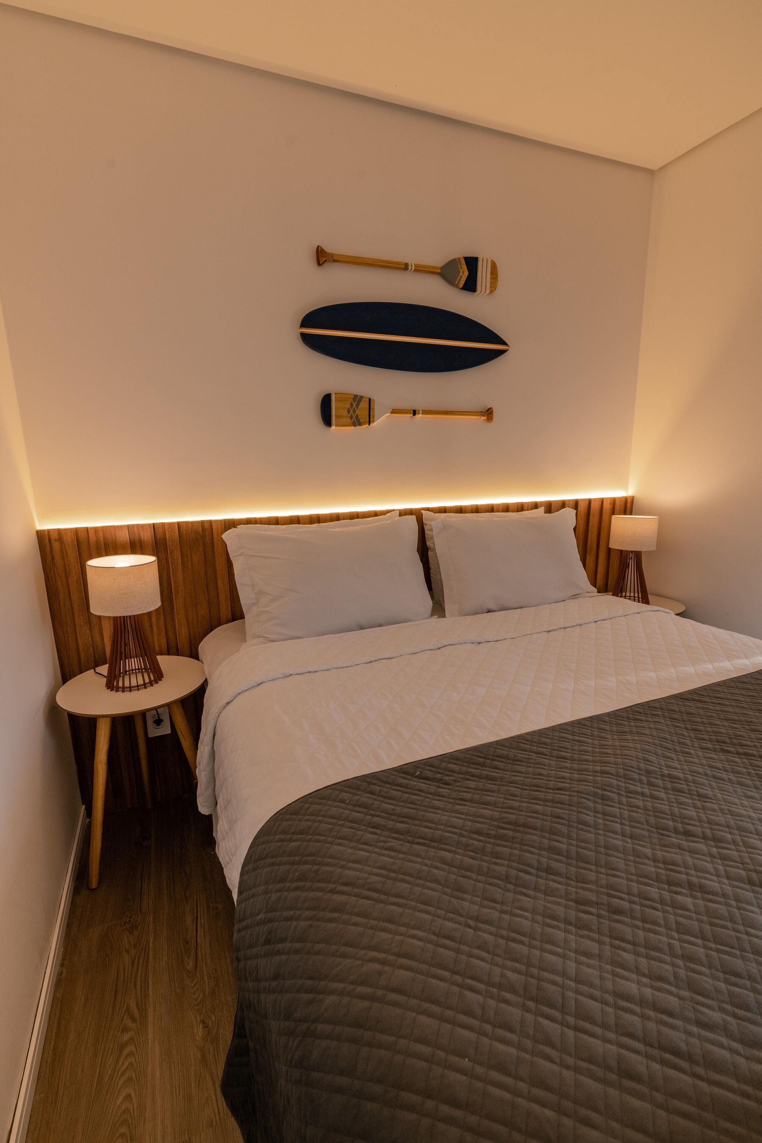 A neatly made bed with white linens, a dark quilted bedspread, and two bedside tables with lamps.