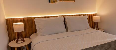 A neatly made bed with white linens, a dark quilted bedspread, and two bedside tables with lamps.