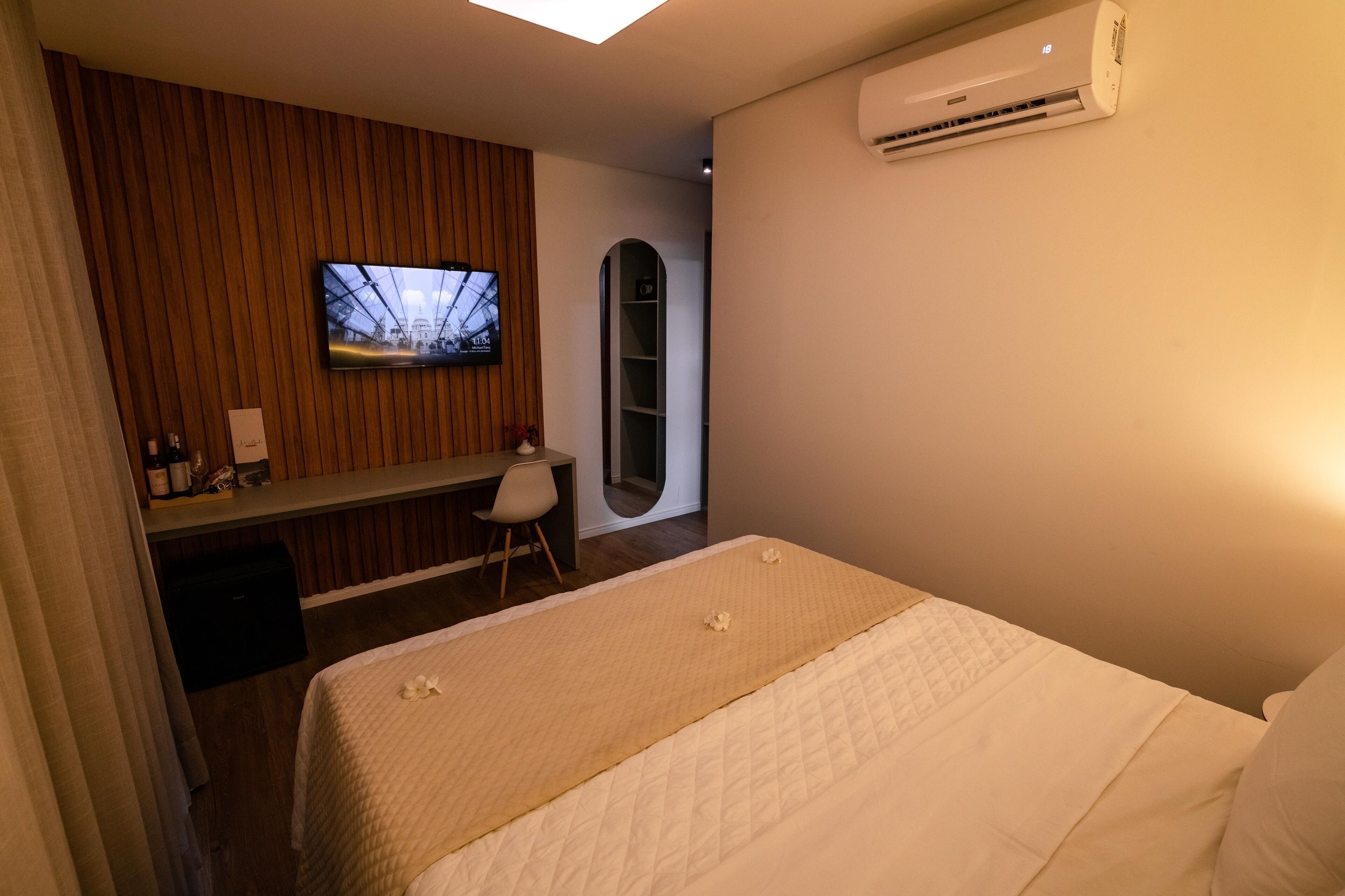 A hotel room with a bed, a desk, a television, and an air conditioning unit.