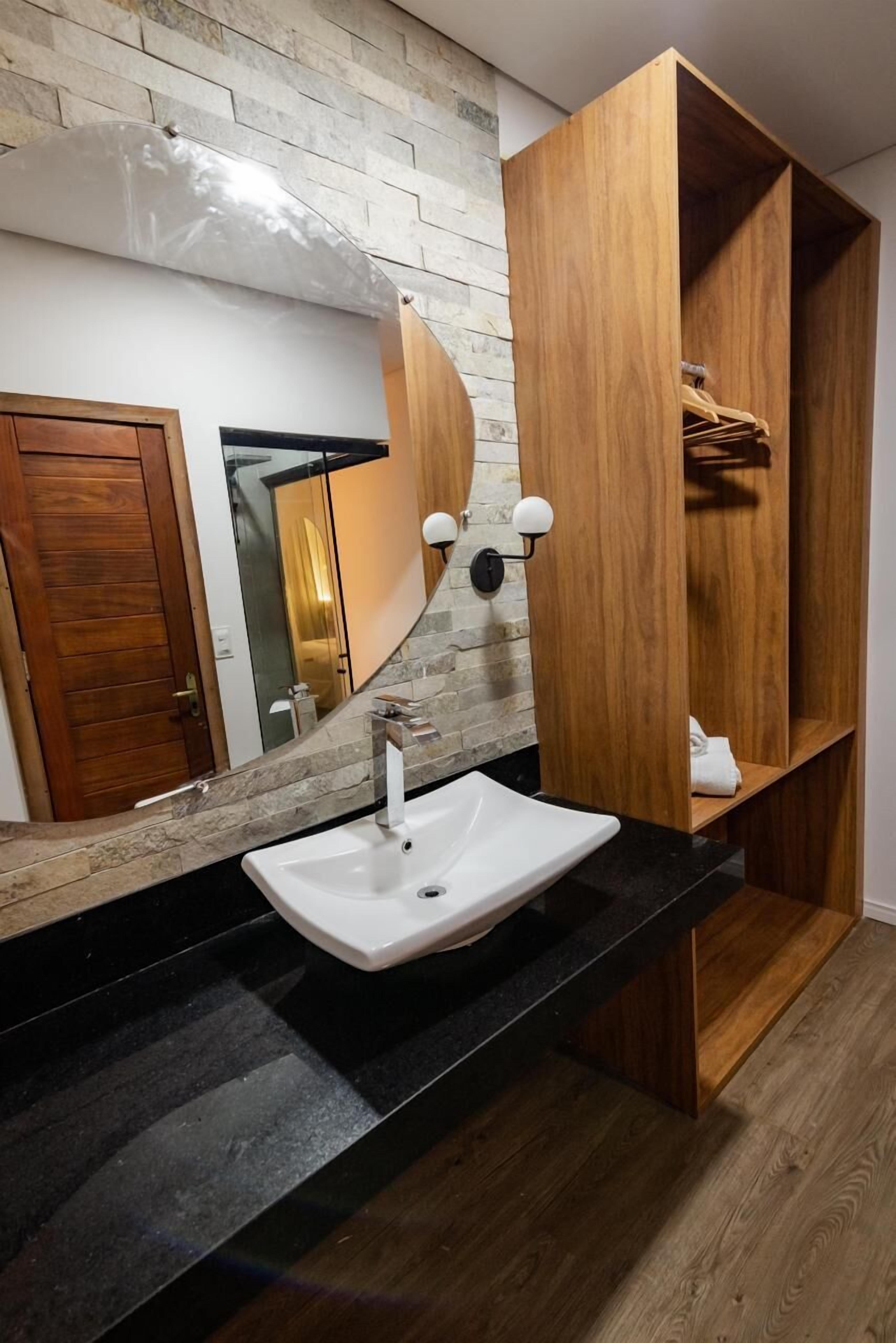 Une salle de bain moderne avec un mur en pierre, un meuble-lavabo en bois, un lavabo blanc et un miroir.