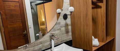 A modern bathroom with a stone wall, a wooden vanity, a white sink, and a mirror.