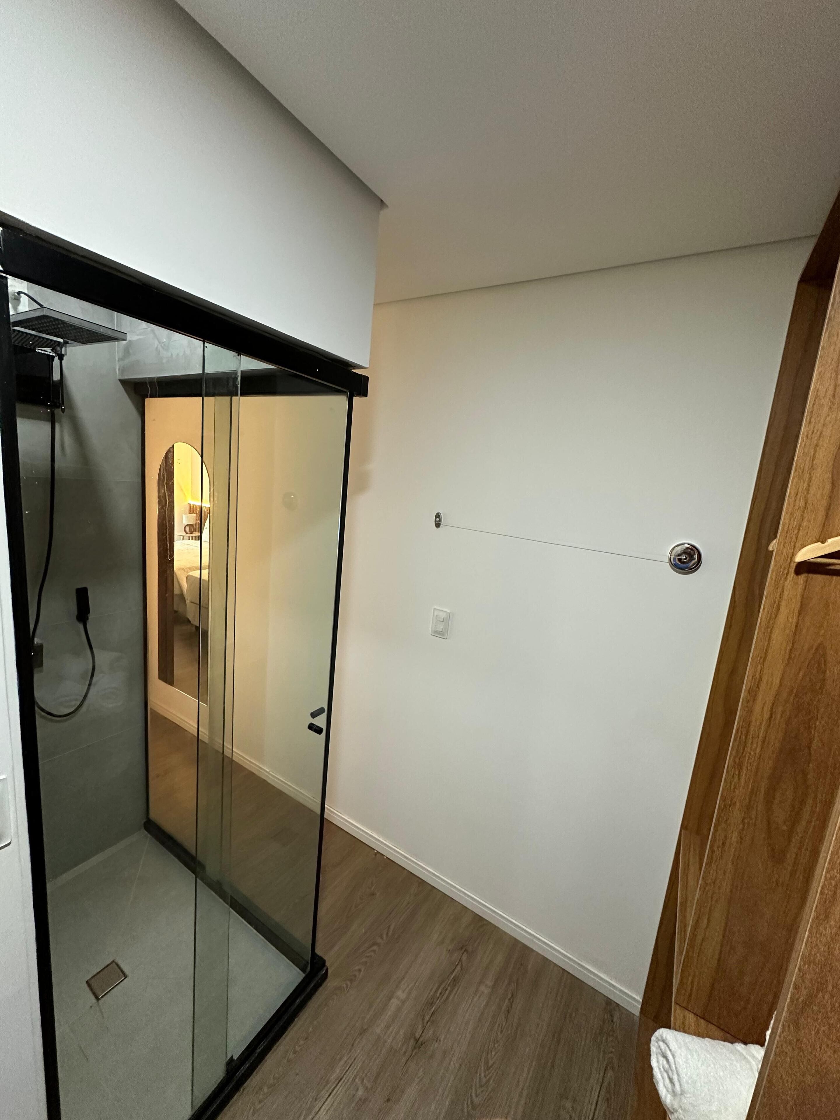 A modern bathroom with a glass shower enclosure, a wooden floor, and a white wall.