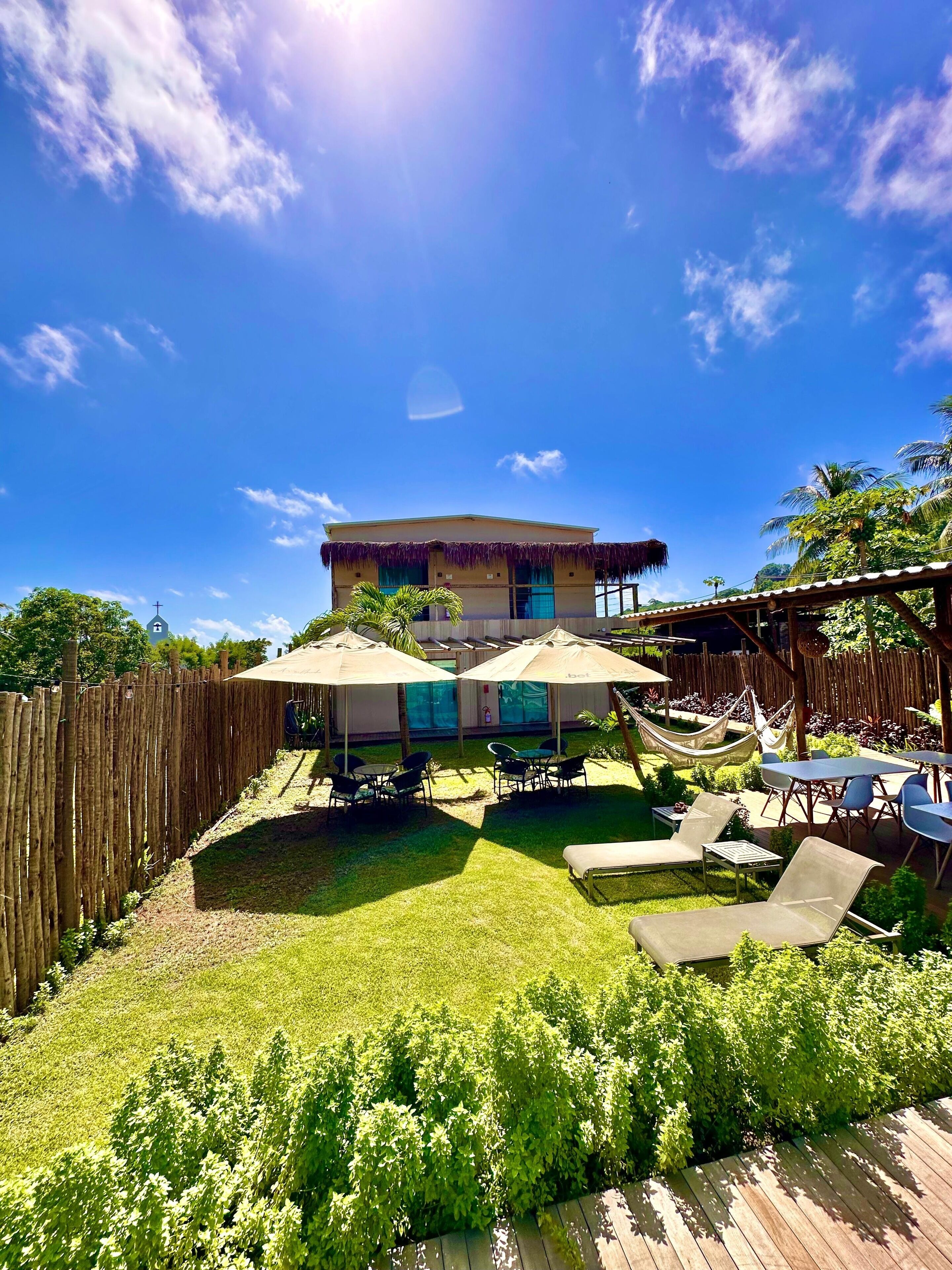 A house with a thatched roof, a fenced yard, outdoor seating, and a hammock.