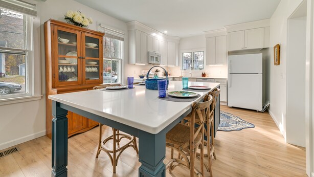 A modern kitchen with white cabinets, a central island with stools, and a view of the outside through large windows.