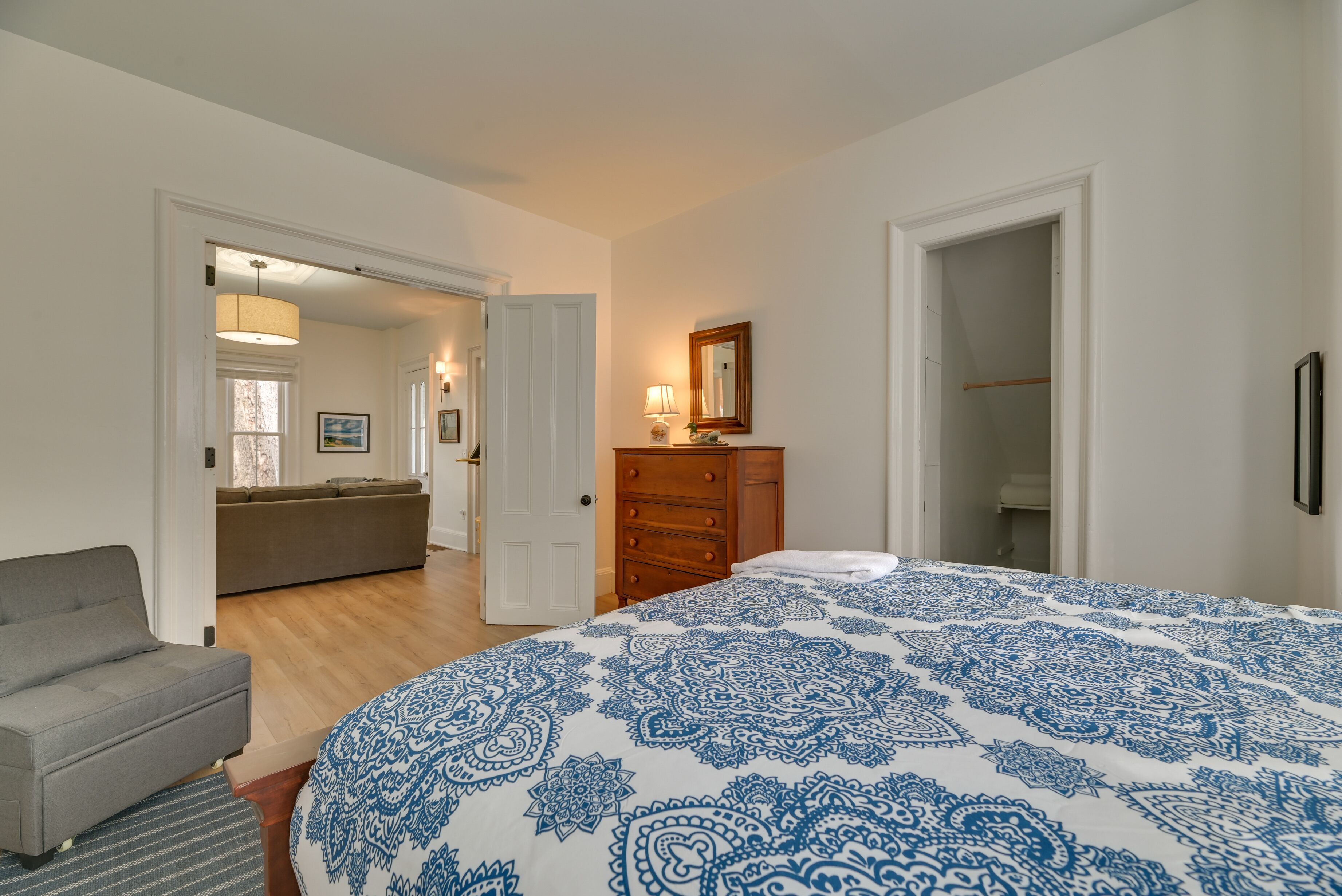 Un dormitorio con una cama grande, un sofá gris, un aparador de madera y un vestidor.