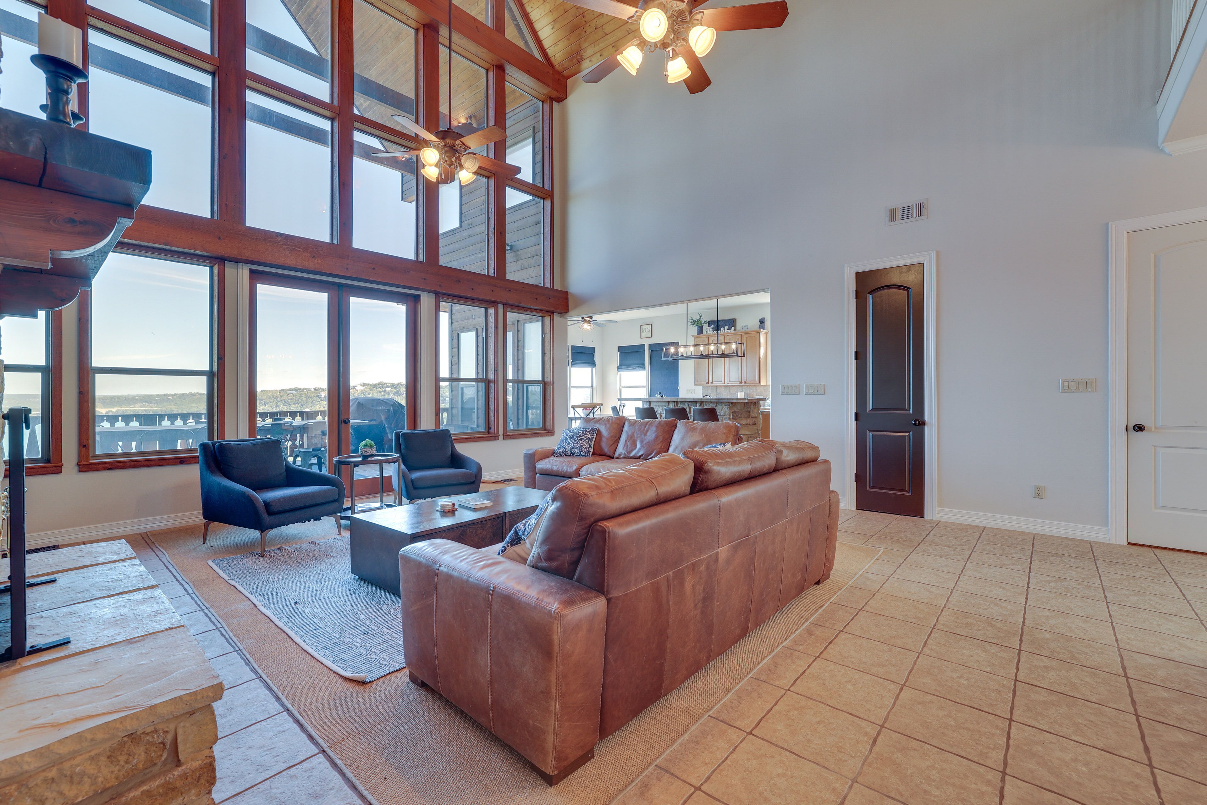 A spacious living room with a large brown leather sofa, a coffee table, and a fireplace. There are large windows offering a view of the city.
