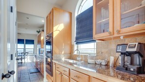 A modern kitchen with wooden cabinets, a built-in oven, a coffee maker, and a large window with blinds. - Scenic Canyon Lake Vacation Home Near Boat Ramp! (Canyon Lake)