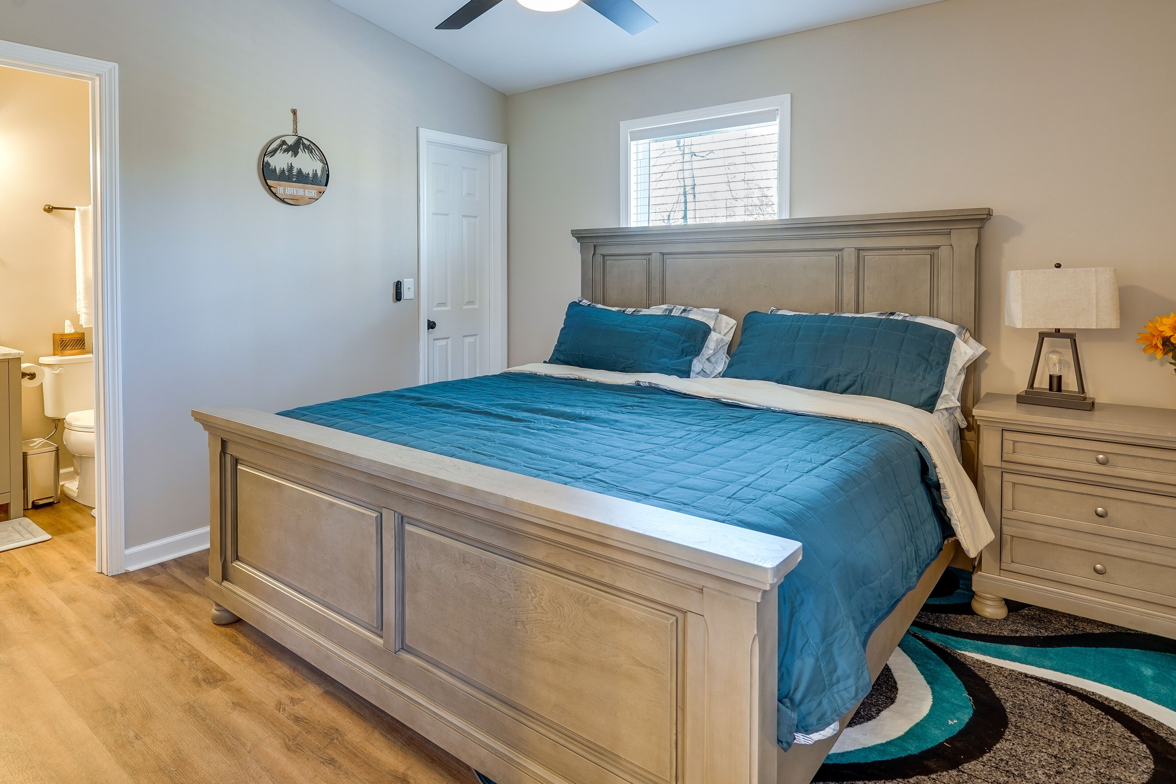 A bedroom with a large bed, a nightstand, a lamp, and a window with blinds.