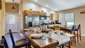 A modern kitchen with wooden cabinets, stainless steel appliances, and a dining area with a wooden table and chairs. - Serene Logan Retreat w/ Hot Tub & Stargazing Dome (Logan)