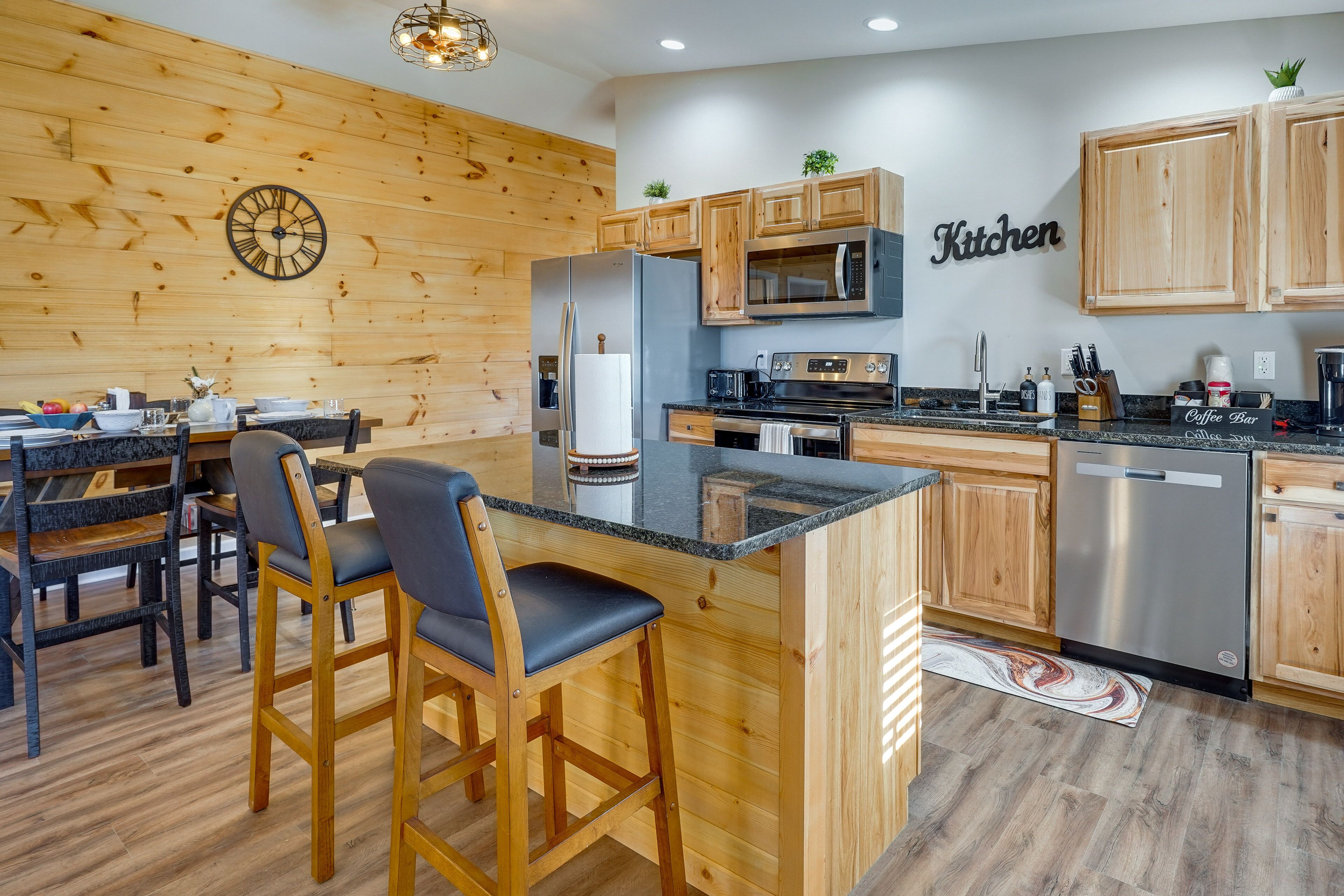 A modern kitchen with wooden cabinetry, a central island, bar stools, and a clock on the wall.
