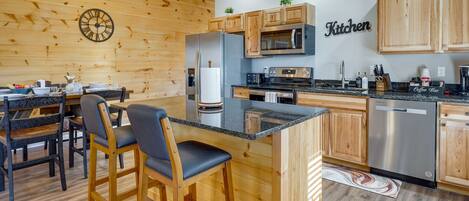 A modern kitchen with wooden cabinetry, a central island, bar stools, and a clock on the wall.