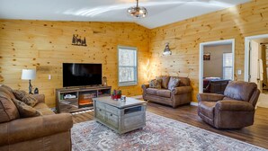 A cozy living room with wooden walls, a flat-screen TV, leather sofas, and a patterned rug. - Serene Logan Retreat w/ Hot Tub & Stargazing Dome (Logan)