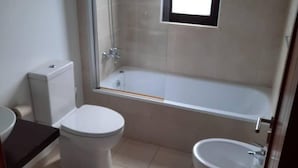 Ein Badezimmer mit Toilette, Bidet, Badewanne und einem Fenster.