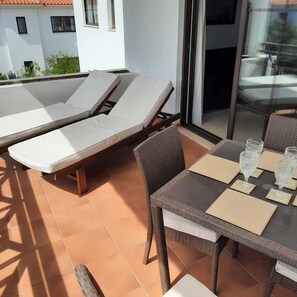 Une terrasse avec deux fauteuils et une table sur laquelle sont posés des verres, donnant sur un immeuble avec des fenêtres.
