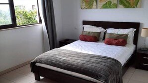 Ein Hotelzimmer mit Bett, Nachttisch, Stuhl und einem Fenster mit Vorhängen.